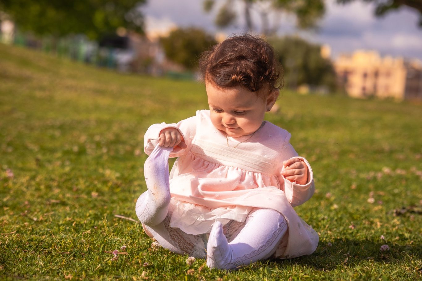Niña pequeña sentada en el césped, jugando con su vestido rosa.