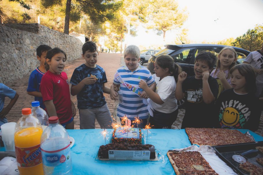 Niños celebrando con un pastel de cumpleaños y globos, sonriendo y disfrutando juntos.