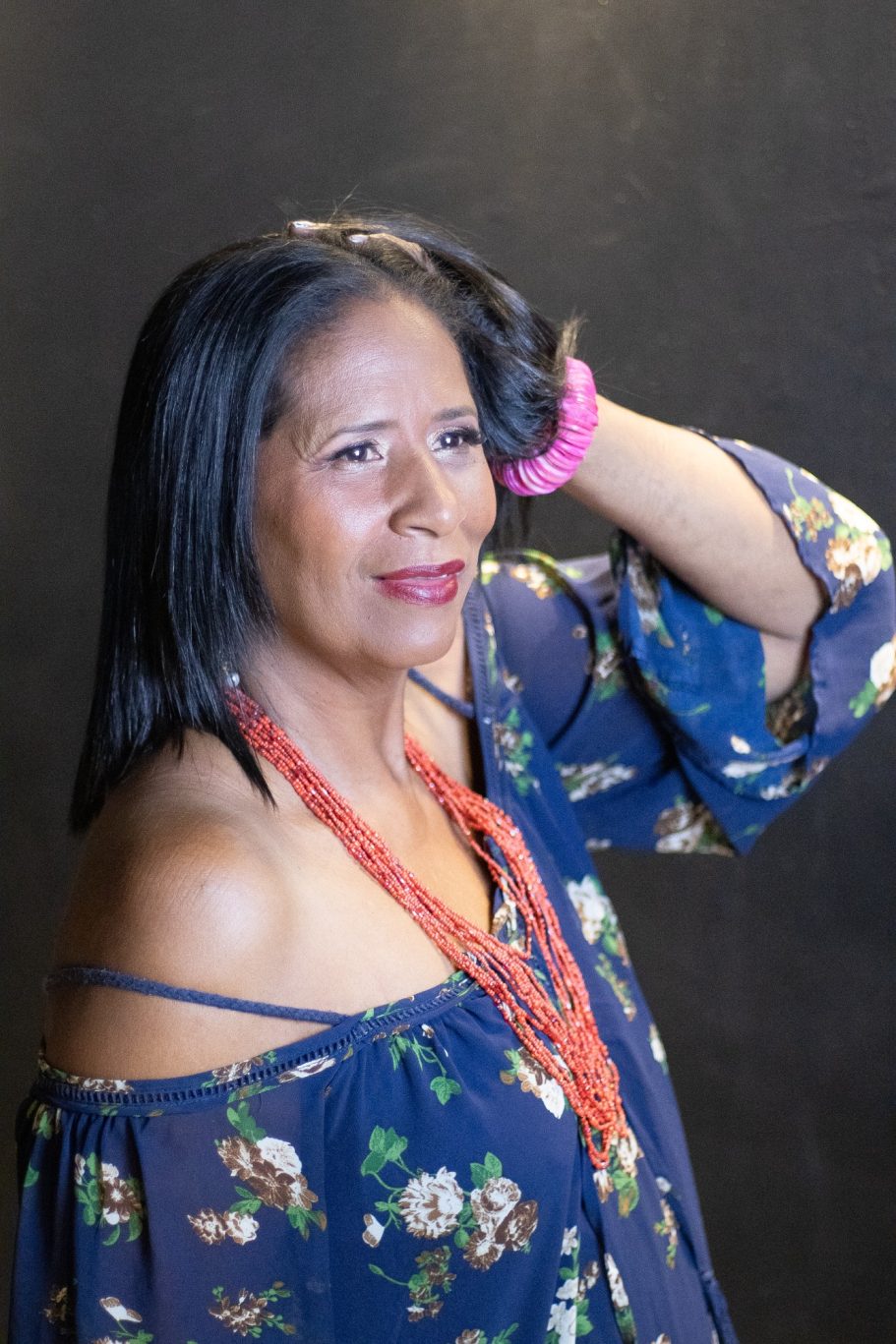 Mujer sonriente con cabello largo y suelto, usando blusa azul y collares de colores.