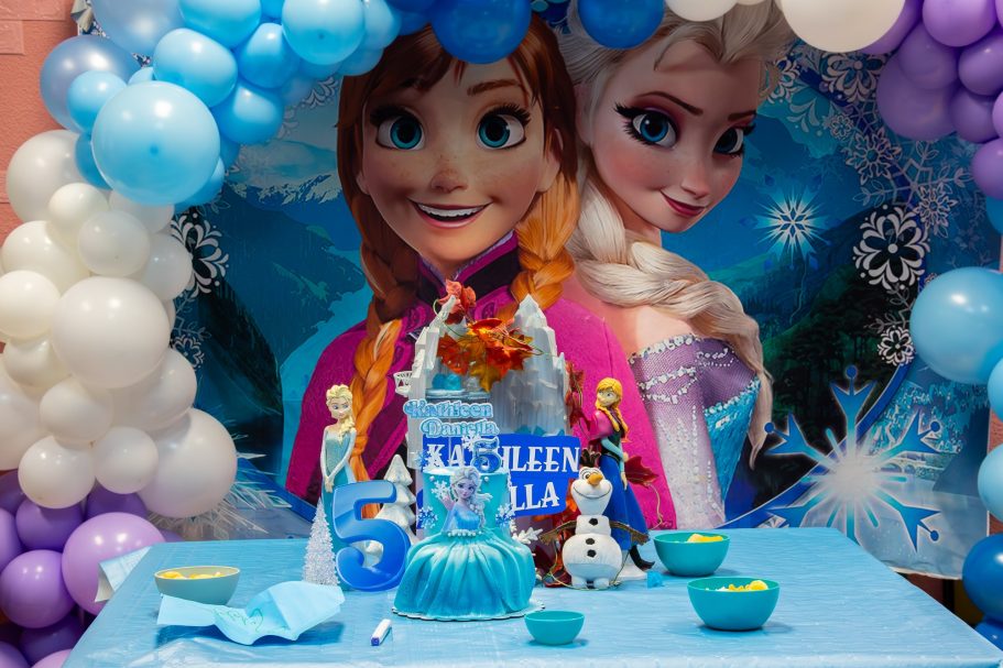 Decoración de fiesta temática "Frozen" con globos, pastel y figuras de Elsa y Anna.