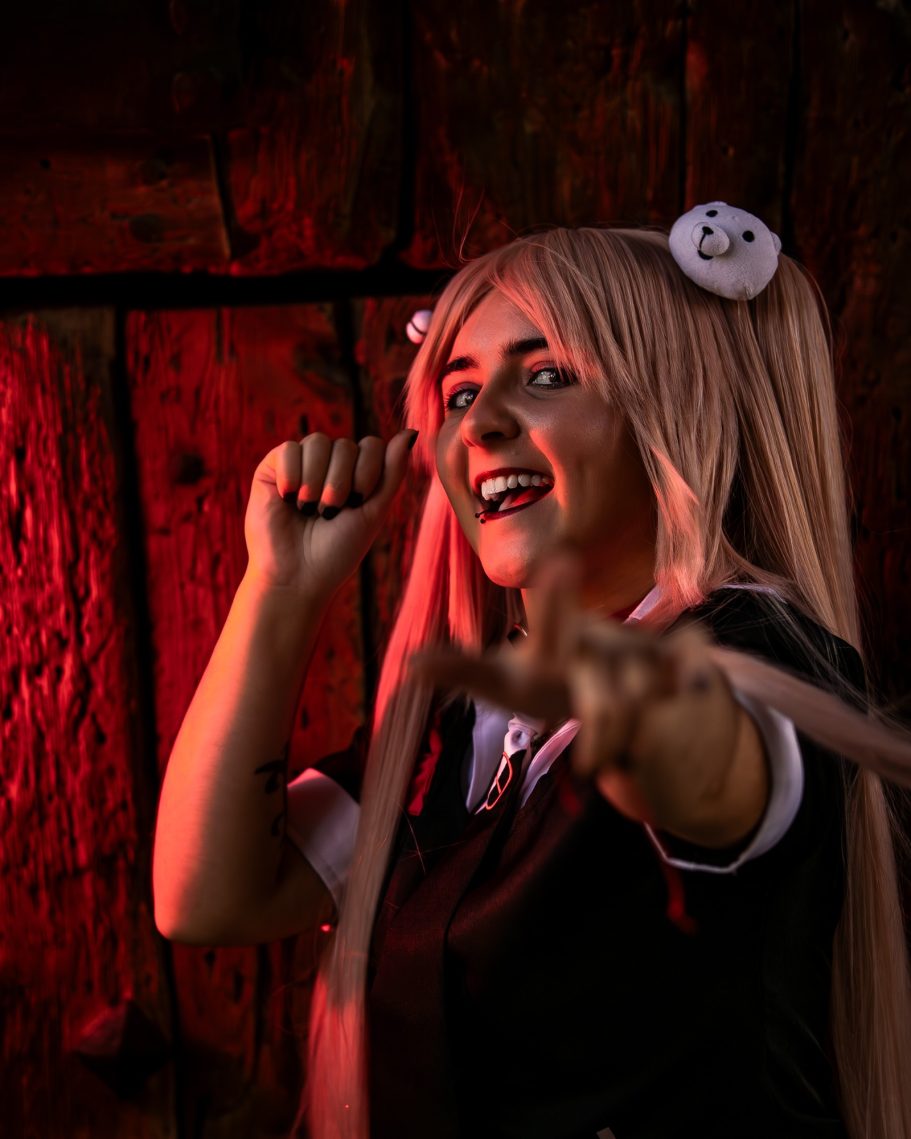 Cosplay de una persona sonriendo con pelo largo y accesorios en un fondo oscuro y rojo.