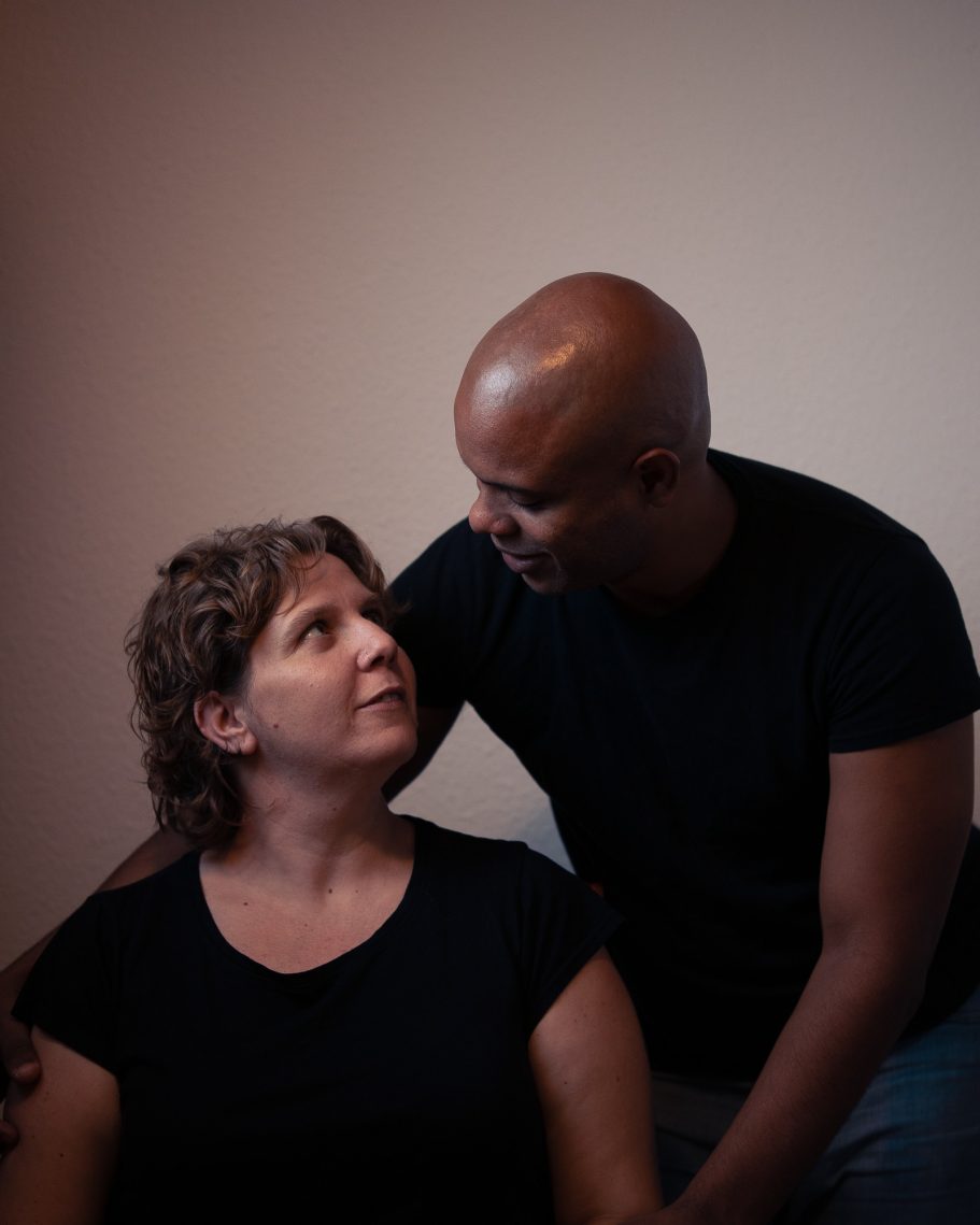 Una mujer y un hombre mirándose con cariño, ambos vestidos con camisetas negras.