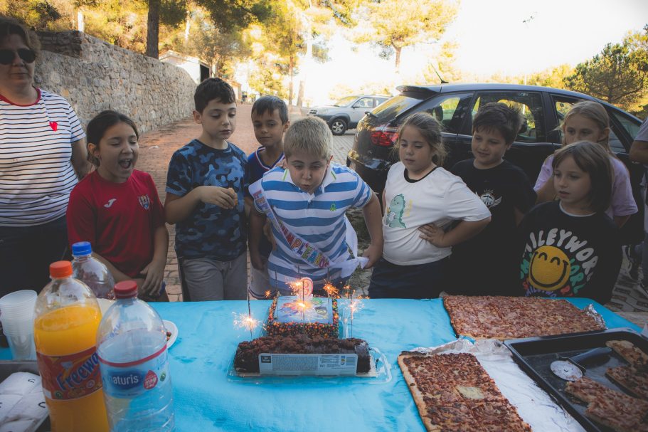 Niño soplando las velas de un pastel rodeado de amigos en una celebración al aire libre.